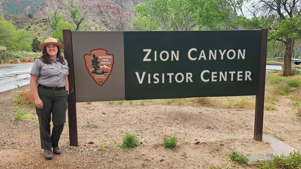 Alumna Rachel Baer in front of Zion Canyon Visitor Center sign.