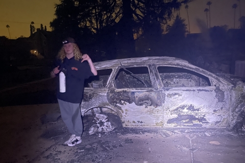 Person standing in front of burnt car in LA