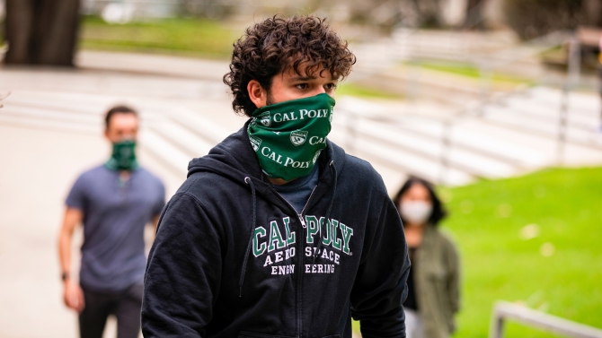 A student wearing a mask walks in front of the library