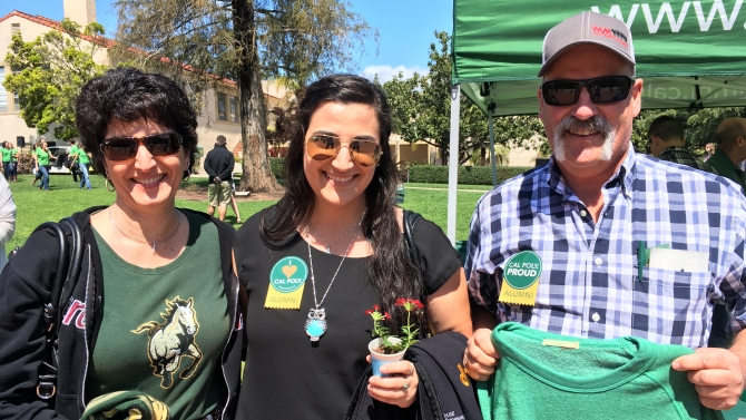 Alumni and student smiling for the camera wearing Cal Poly clothing.