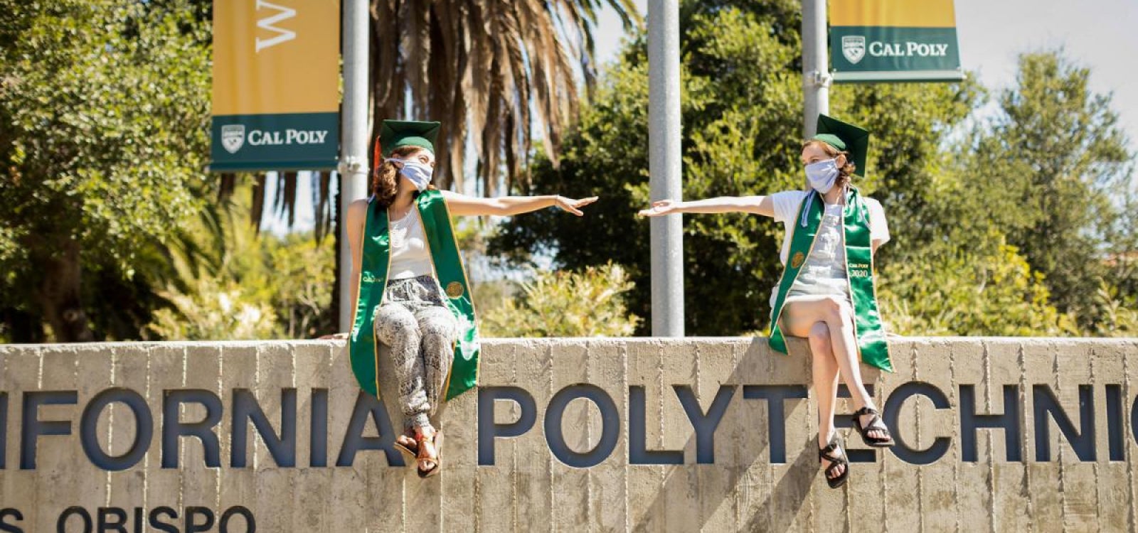 Cal Poly grads wearing masks sitting on campus signage