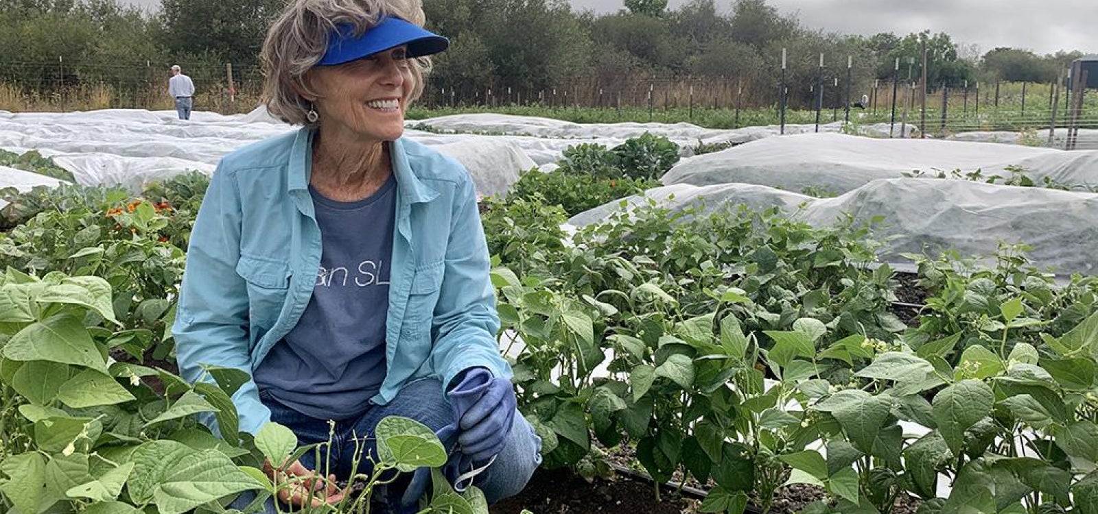 Alum Susan McTaggart kneels in a field, smiling into the distance