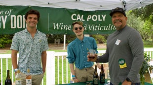 Alumni and students pose in front of a wine tabling booth.