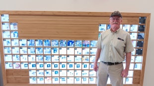 Alum Mark Kent standing in front of the periodic table at the Cal Poly San Luis Obispo campus.