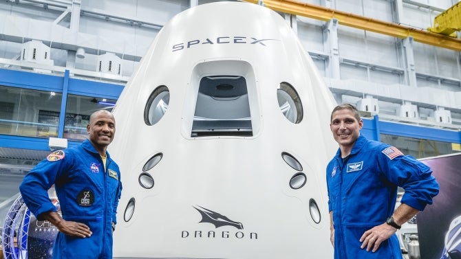 Victor Glover and Mike Hopkin pose in front of their spacecraft at NASA's Johnson Space Center in Houston in 2018, ahead of the agency's announcement of their commercial crew assignment. 