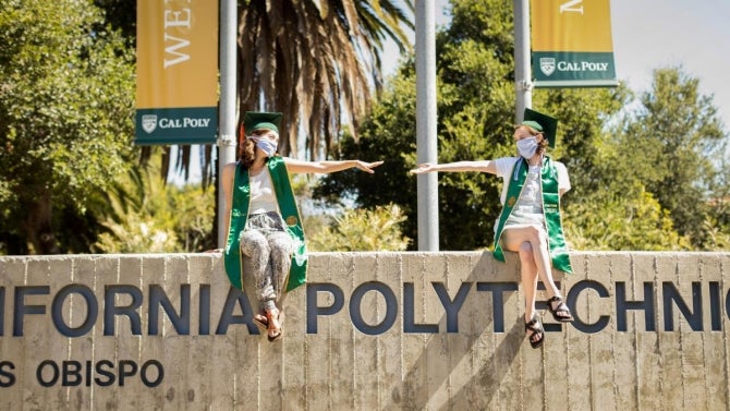 Cal Poly grads wearing masks sitting on campus signage