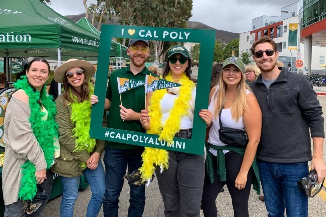 Alumni smiling for the camera with Cal Poly props. 