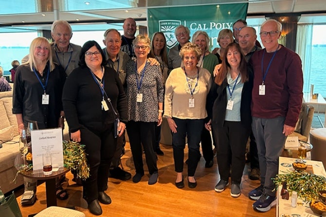 Cal Poly Alumni smiling in front of Cal Poly flag