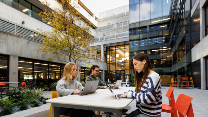 Three people sitting at a table and working in the courtyard of the Robert E. Kennedy Library