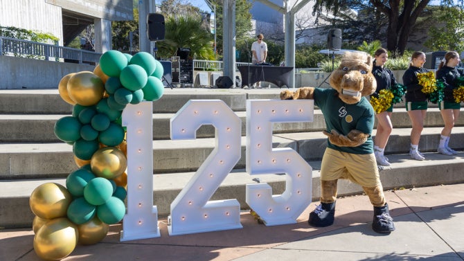Cal Poly Mascot "Musty" poses for a picture in front of the 125-year anniversary sign. 