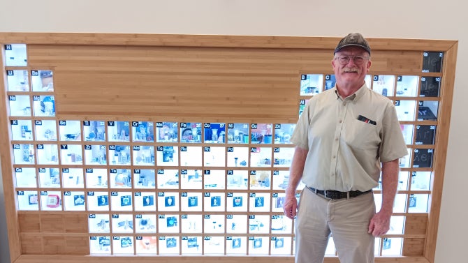 Alum Mark Kent standing in front of the periodic table at the Cal Poly San Luis Obispo campus.