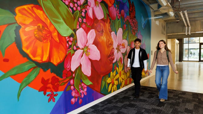 Students walking inside Kennedy Library next to a mural.